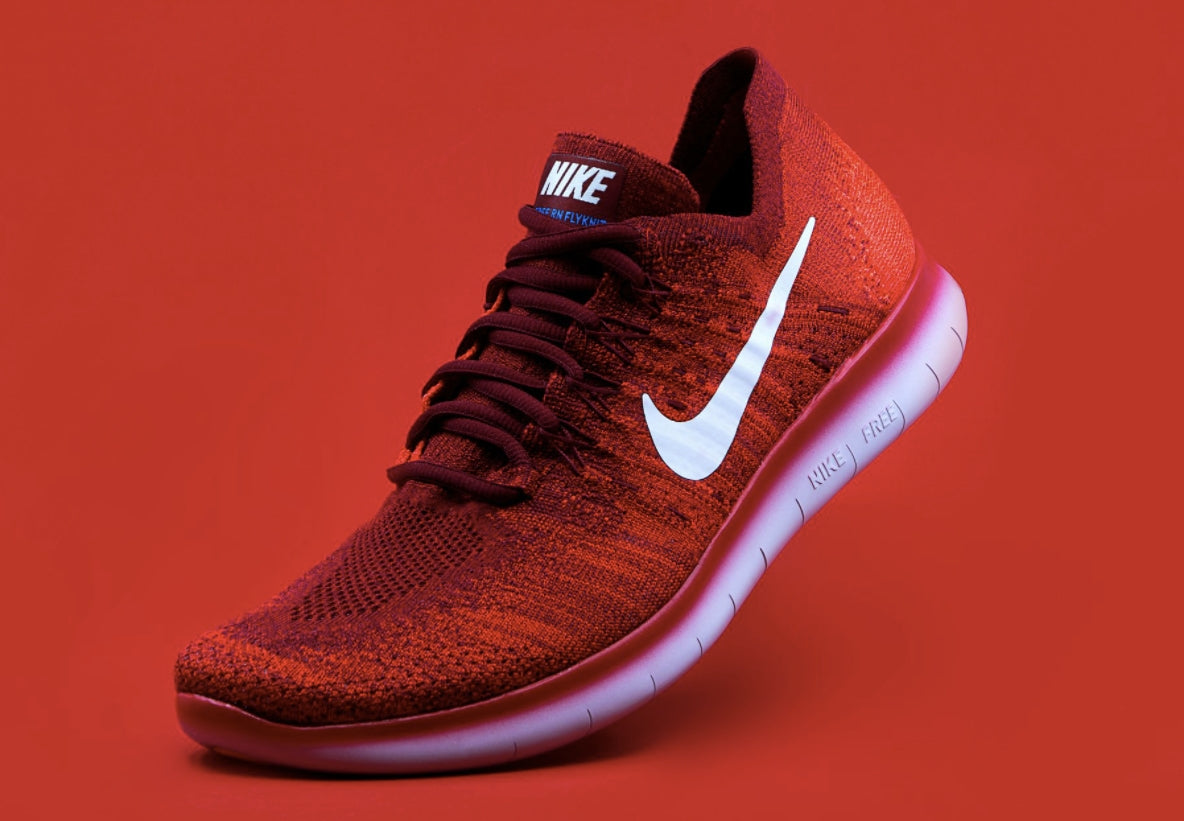 Nike Fly Knit low-top runner in Fire Red, three-quarter view showing the swoosh on the outside of the left shoe.