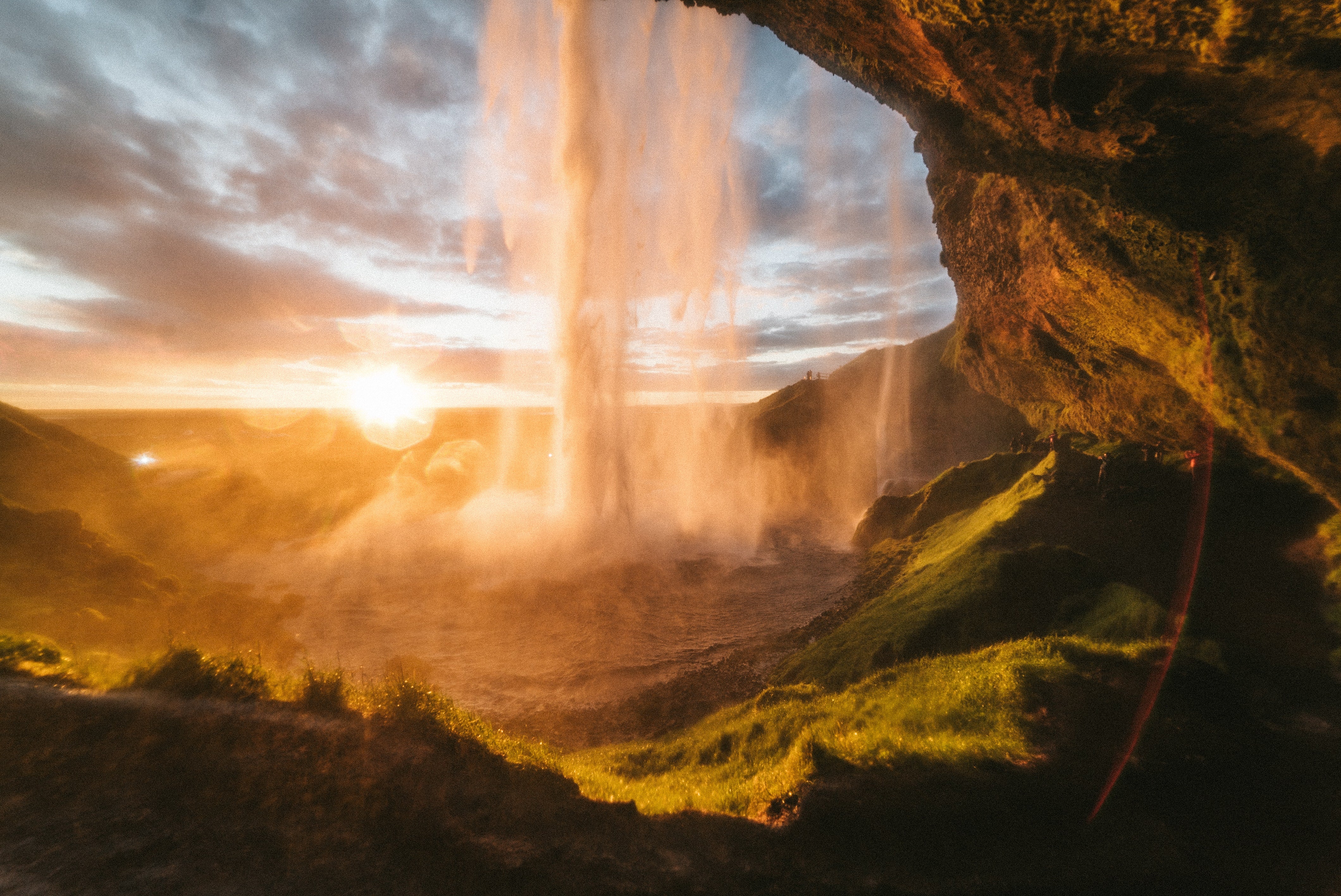 An example photo of a waterfall. It was taken at sunset from the rear of the water with a rocky outcropping overhead in the top corner, and the overall tone is warm oranges and greens.